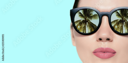 Portrait close up of a pretty woman with reflection of palms in sunglasses  on a bright background