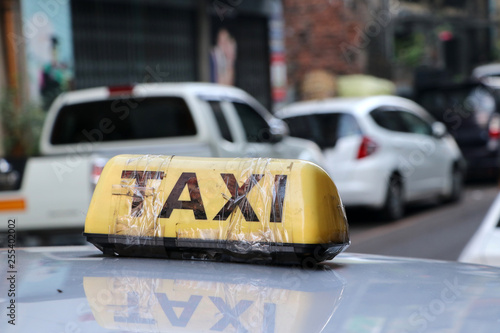 Taxi light sign or cab sign in yellow color with black text and tied with transparent tape on the car roof at the street blurred background.