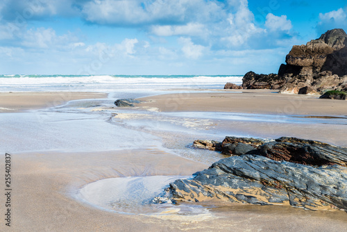 A fresh bright and breezy day in a quiet sandy cove on the North Cornish coast, England UK, with sand, pools and rocks in the foreground.