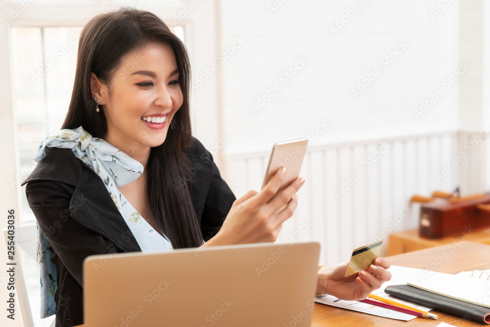 Young asian woman holding credit card and using laptop computer for purchase product on internet in home office. Online shopping concept. Young asian woman holding credit card and using laptop computer for purchase product on internet in home office. Online shopping concept.
