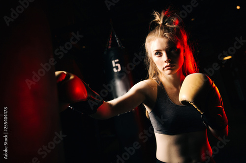 Blonde athlete in boxing gloves hits bag in training.
