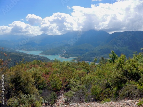 Mountains covered with green forest against the blue sky and snow-white clouds. a river with turquoise water in the distance