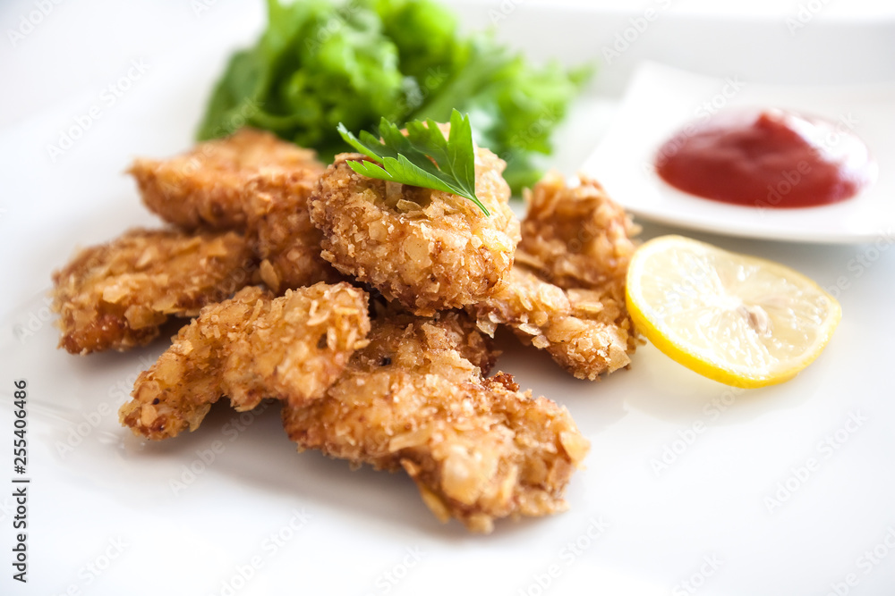 close-up of delicious crispy fried chicken breast strips on white plate, Chicken nuggets with cornflakes salad and Ketchup close-up of delicious crispy fried chicken breast strips on white plate, Chicken nuggets with cornflakes salad and Ketchup