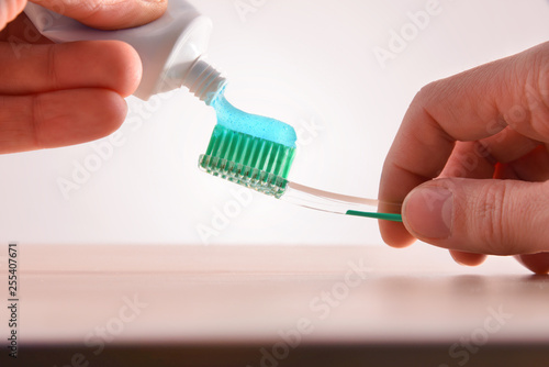 Hands with tube and geen toothbrush putting toothpaste