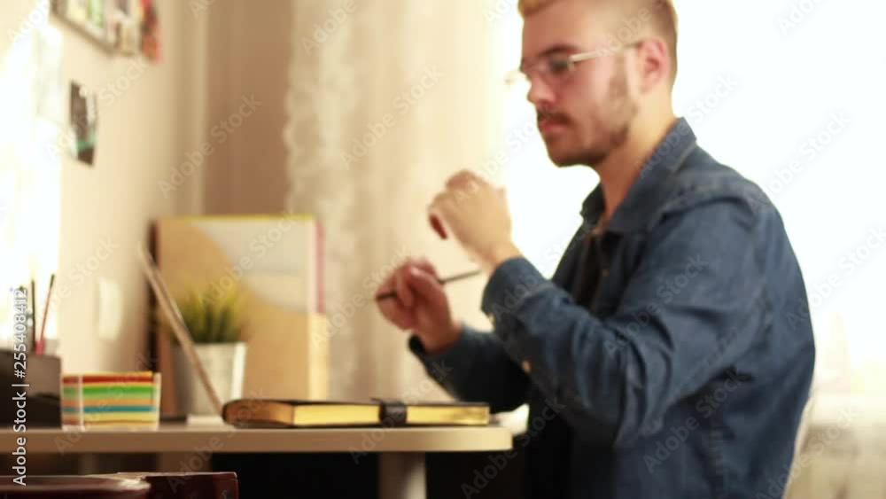 Side view of focused male entrepreneur sitting at table with laptop in cozy workspace and working on startup project while writing on sticky notes Side view of focused male entrepreneur sitting at table with laptop in cozy workspace and working on startup project while writing on sticky notes