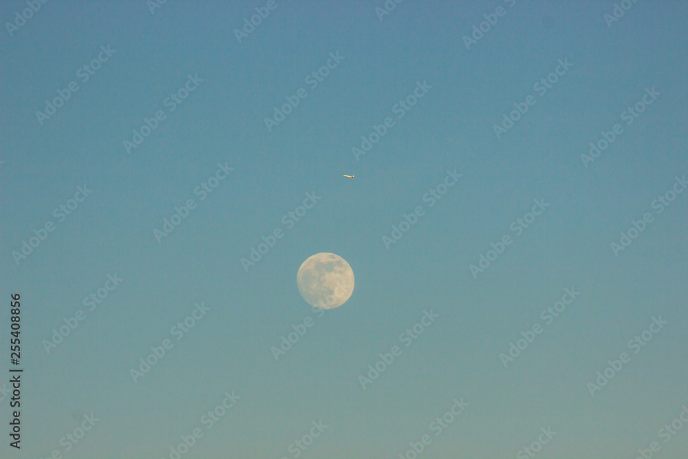 the moon against the blue sky and next to the plane flies. it was getting dark, the sunset and the moonrise. day and night change the moon against the blue sky and next to the plane flies. it was getting dark, the sunset and the moonrise. day and night change