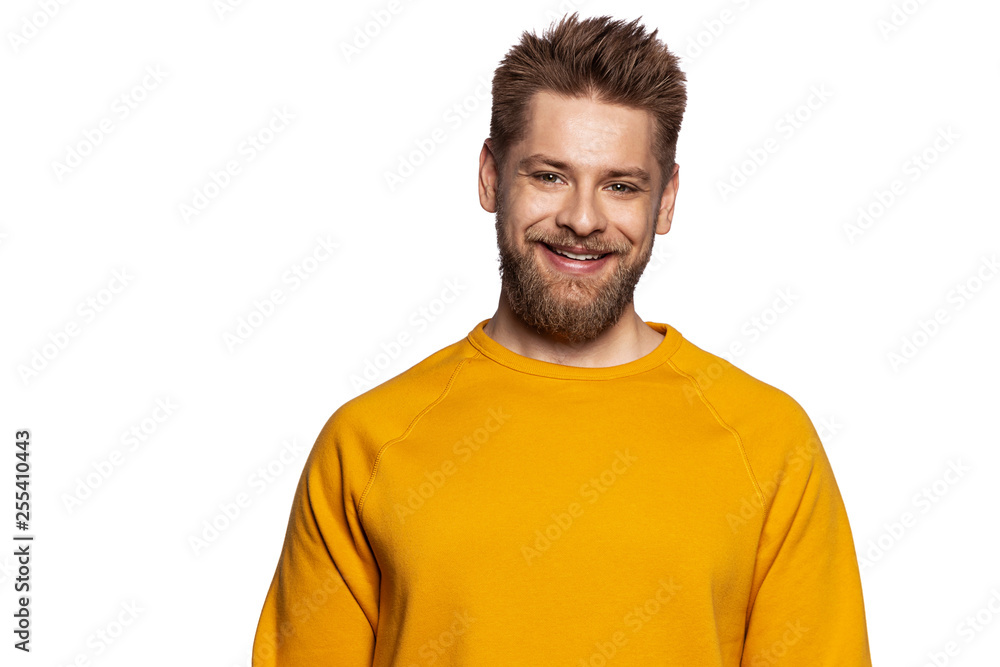 Fototapeta premium Cute guy in a stylish bright sweatshirt stands on an isolated white background and smiling looks at the camera