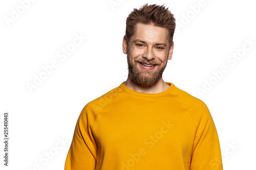 Cute guy in a stylish bright sweatshirt stands on an isolated white background and smiling looks at the camera