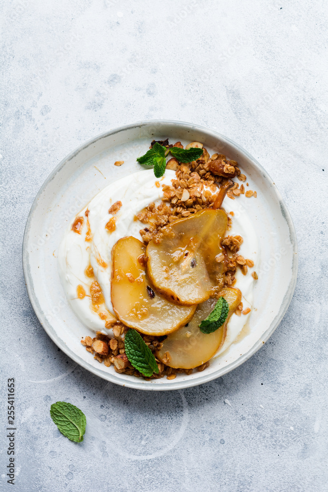 Greek yogurt with caramelized pear, granola, nuts and melted sugar for a wholesome breakfast on a gray ceramic plate. Rustic style. Top view. Greek yogurt with caramelized pear, granola, nuts and melted sugar for a wholesome breakfast on a gray ceramic plate. Rustic style. Top view.