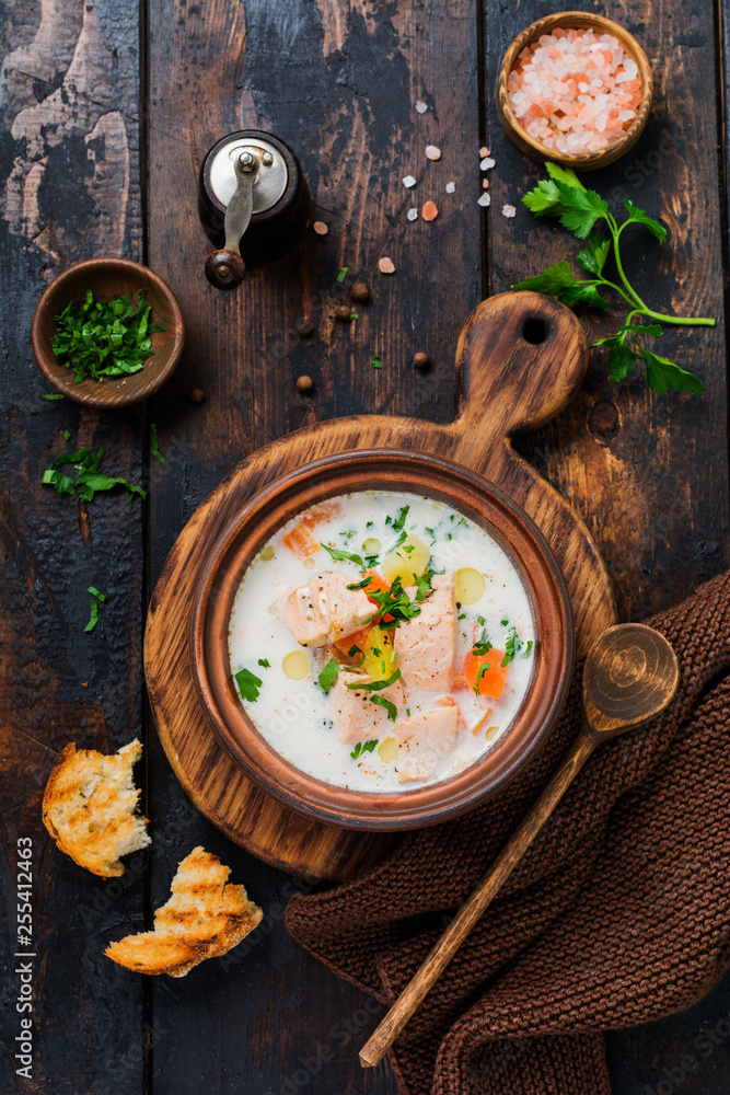Warm Finnish creamy soup with salmon and vegetables in old ceramic bowl on old wooden background. Rustic style. Top view.