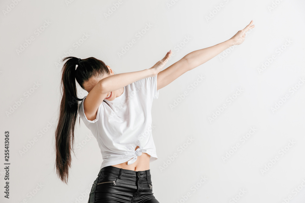 Young woman makes a dab movement with arms on a gray background. Human emotions, facial expression concept. Young woman makes a dab movement with arms on a gray background. Human emotions, facial expression concept.