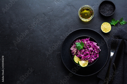 Salad of purple Peking cabbage with olive oil, lime and black sesame seeds in ceramic plate on dark concrete background.