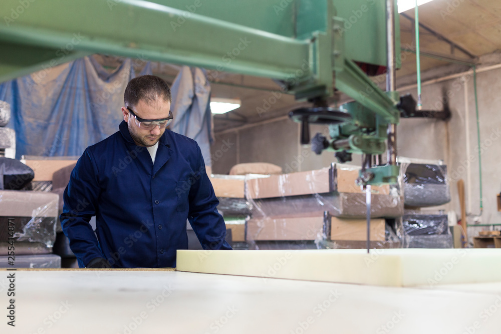 Young man in a furniture factory is cutting the foam for the sofa Young man in a furniture factory is cutting the foam for the sofa