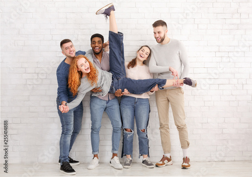 Students holding friend and having fun over brick wall