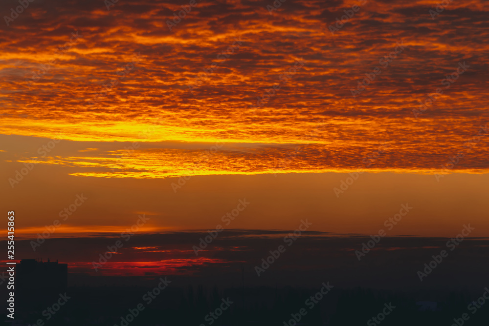 Cityscape with vivid fiery dawn. Amazing warm dramatic cloudy sky above dark silhouettes of city building roofs. Orange sunlight. Atmospheric background of sunrise in overcast weather. Copy space. Cityscape with vivid fiery dawn. Amazing warm dramatic cloudy sky above dark silhouettes of city building roofs. Orange sunlight. Atmospheric background of sunrise in overcast weather. Copy space.
