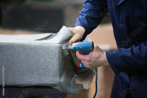 Closeup of a young man in a furniture factory who puts together one part of the sofa with a stapler photo