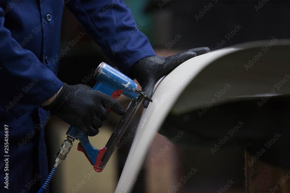 Closeup of a young man in a furniture factory who puts together one part of the sofa with a stapler Closeup of a young man in a furniture factory who puts together one part of the sofa with a stapler
