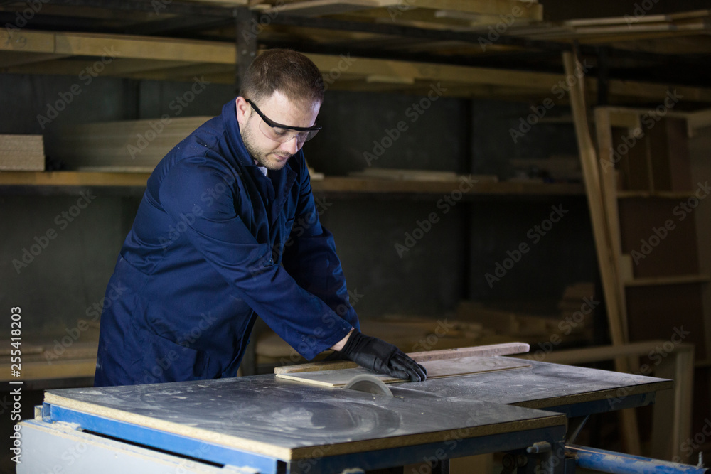 Young man in a furniture factory cutting the wooden pieces for the sofa