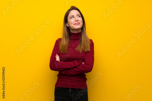 Woman with turtleneck over yellow wall looking up while smiling