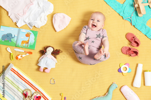 Cute little baby with clothing and accessories on color blanket, top view