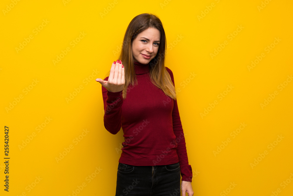 Woman with turtleneck over yellow wall inviting to come with hand. Happy that you came Woman with turtleneck over yellow wall inviting to come with hand. Happy that you came