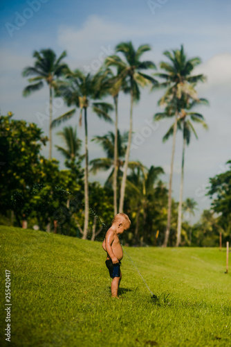 small baby playing in aweome park on background of tropical palms and blue sky in Bali