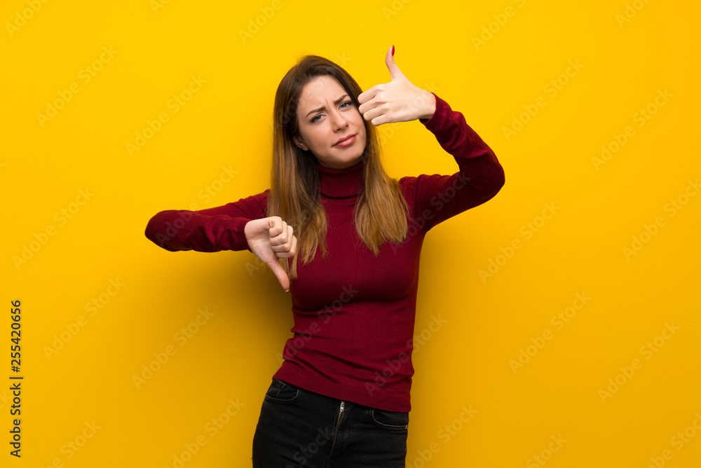 Woman with turtleneck over yellow wall making good-bad sign. Undecided between yes or not Woman with turtleneck over yellow wall making good-bad sign. Undecided between yes or not