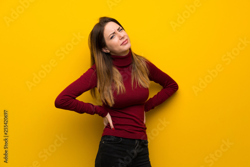 Woman with turtleneck over yellow wall suffering from backache for having made an effort © luismolinero