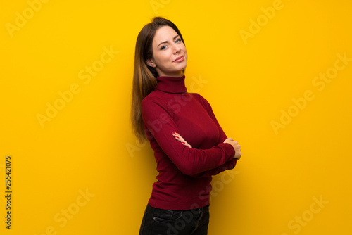 Woman with turtleneck over yellow wall with arms crossed and looking forward