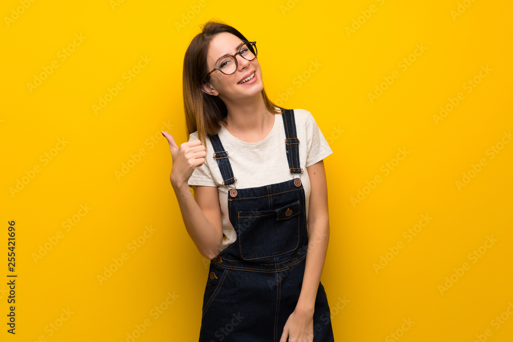 Fototapeta premium Woman over yellow wall with thumbs up because something good has happened