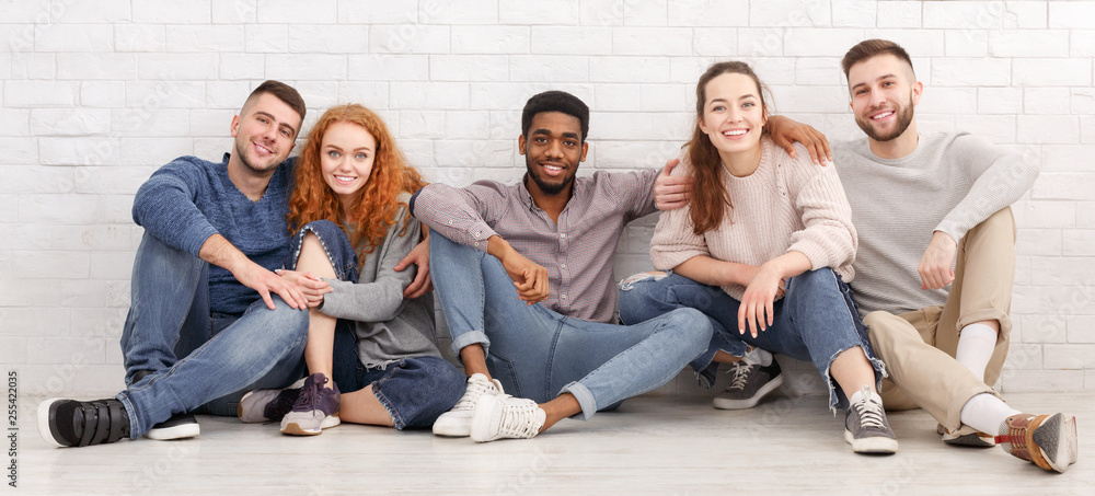 Diverse friends hugging, sitting on floor over light wall