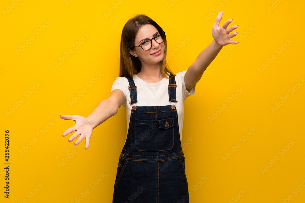 Woman over yellow wall presenting and inviting to come with hand Woman over yellow wall presenting and inviting to come with hand