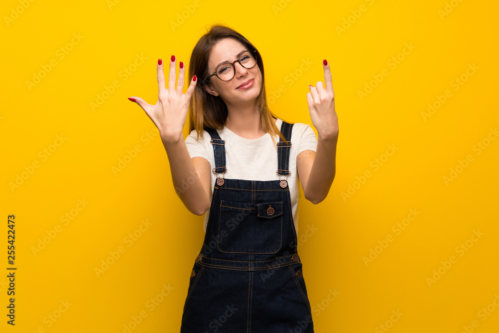 Woman over yellow wall counting six with fingers Woman over yellow wall counting six with fingers