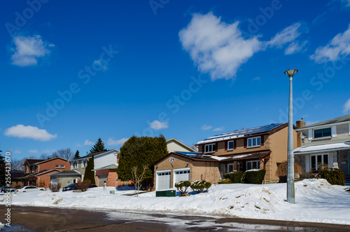 Winter scene of a row of residential houses, one with solar panels on the roof.