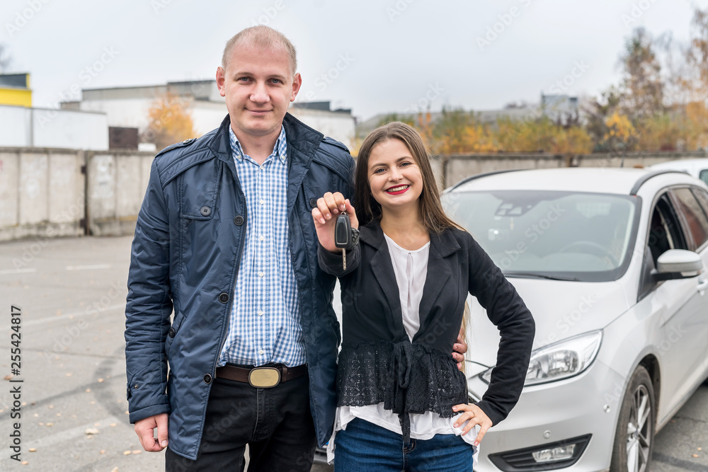 Smiling couple posing near new car with keys Smiling couple posing near new car with keys