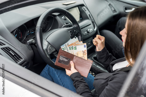 Woman showing euro banknotes in wallet sitting in car