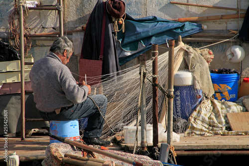 Fotografie Fisherman repairing his net in the afternoon hours