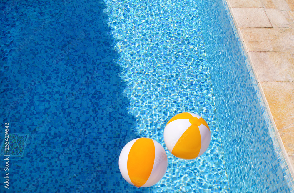 Two rubber air yellow white inflatable balls and toy for swimming pool in transparent blue water. Multi-colored beach balls floating on water in blue swimming pool for concept relax holiday travel.