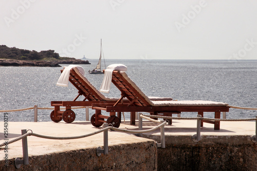 Private beaches on mediterranean sea. Chairs, deck chairs, sun loungers and parasols waiting for tourists. Tiny secluded rocky beach with lush vegetation of olive trees and swimming area at ocean.