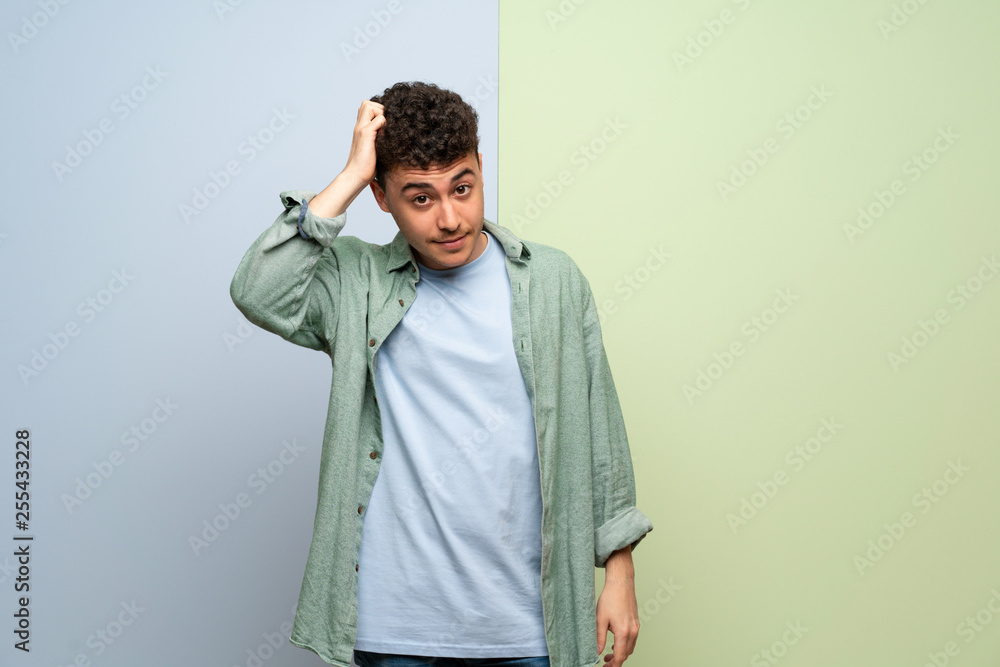 Young man over blue and green background with an expression of frustration and not understanding Young man over blue and green background with an expression of frustration and not understanding