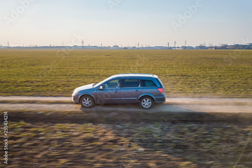 Fototapeta Naklejka Na Ścianę i Meble -  Aerial view of car driving by straight ground road through green fields on sunny blue sky copy space background. Drone photography.