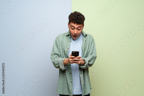 Young man over blue and green background surprised with a mobile © luismolinero