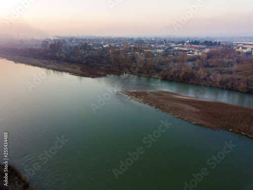 Aerial top view, countryside panorama of quiet river water and island with dry grass, misty horizon under blue sky on sunny day. Drone photography.
