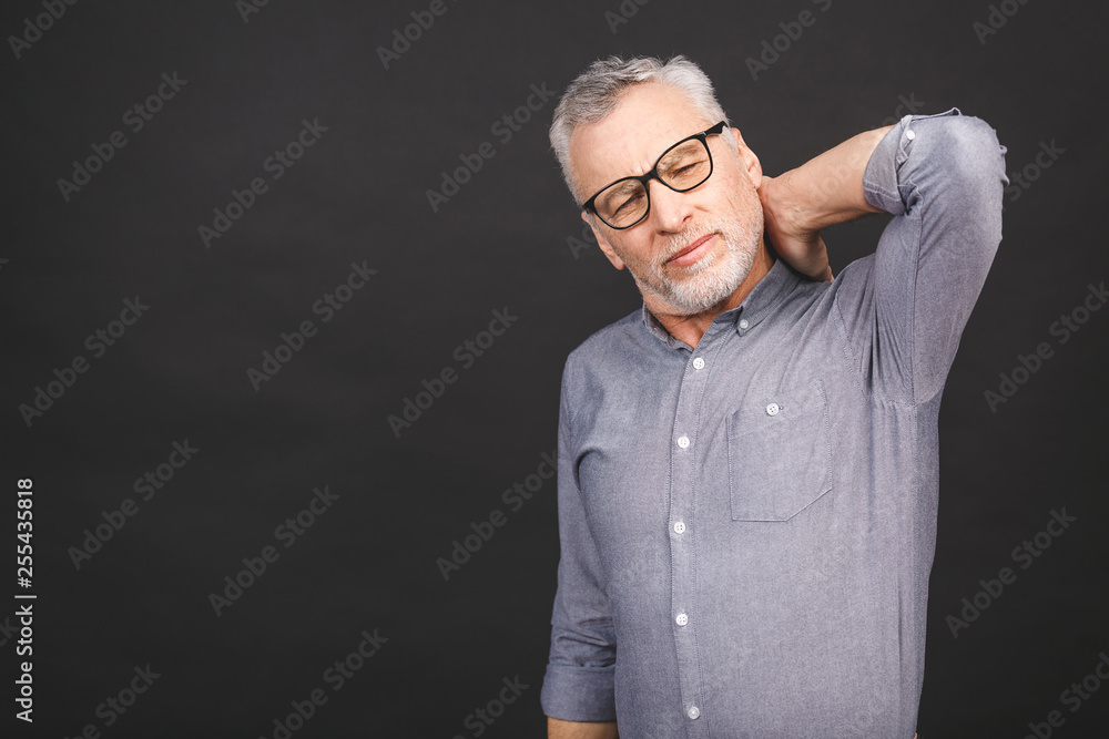 I need a massage. Frustrated senior man in smart casual clothing holding hand on his neck while standing against black background. I need a massage. Frustrated senior man in smart casual clothing holding hand on his neck while standing against black background.