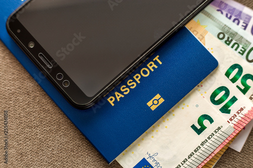 Modern black cellphone, Euro money banknotes bills and travel passport on copy space background. Travelling light, comfortable journey concept.