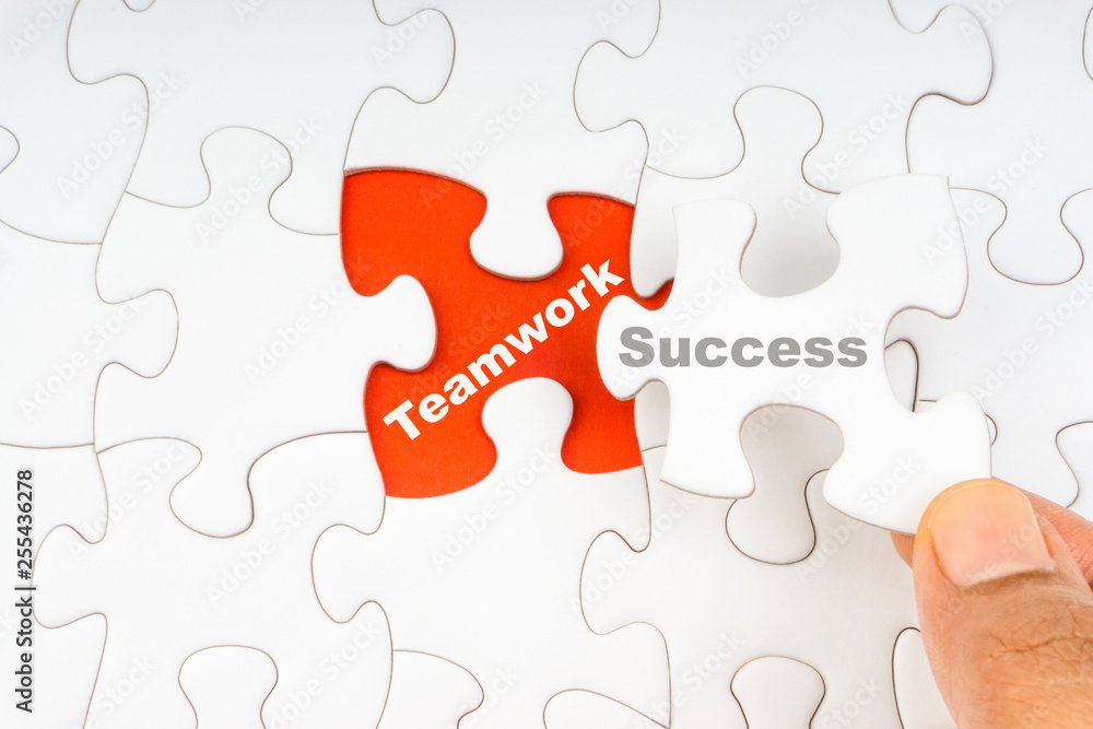 Fototapeta premium Hand holding piece of jigsaw puzzle with word SUCCESS TEAMWORK. Selective focus