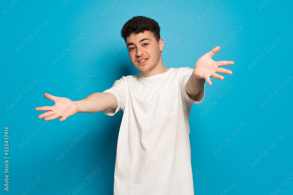 Young man over blue background presenting and inviting to come with hand Young man over blue background presenting and inviting to come with hand