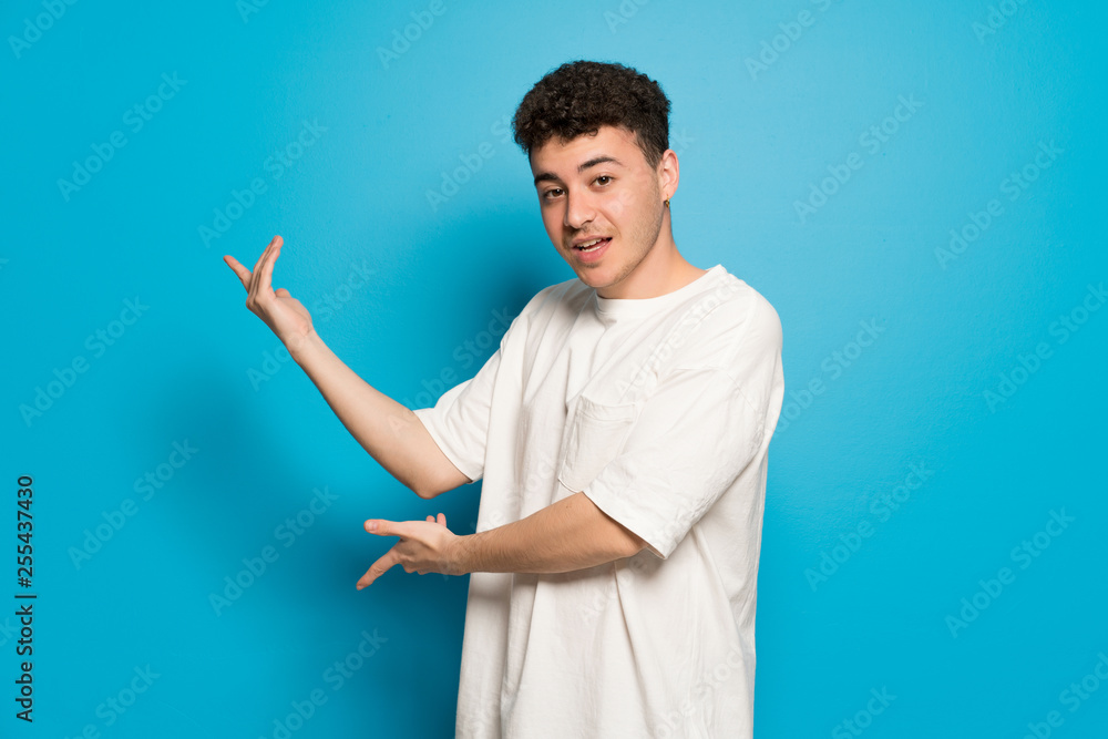 Young man over blue background extending hands to the side for inviting to come