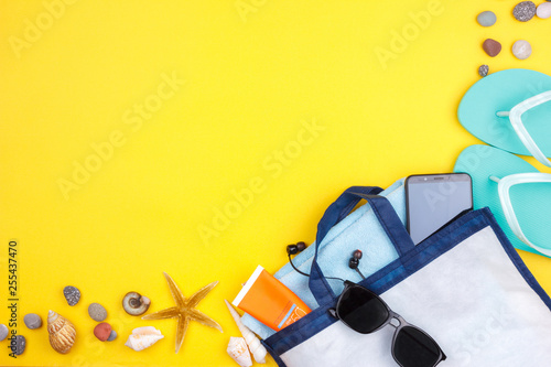 Sun glasses, sun screen, headphones, smartphone, towel, slippers. Flatlay beach vacation on a yellow background.