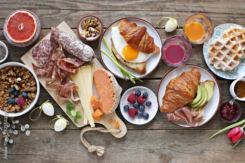 Easter festive brunch or breakfast set, meal variety with fried egg, sausage and cheese variety, croissants, granola, smoothie and dessert. Overhead view